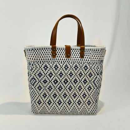 Bolsa artesanal grande color blanco, tejida a mano con toquilla obtenida del reciclado de plástico y detalles en piel sintética color marrón. Diseño exclusivo con textura geométrica, ideal para uso diario o como accesorio de moda sostenible, hecho en México con material plástico reciclado, toquilla.