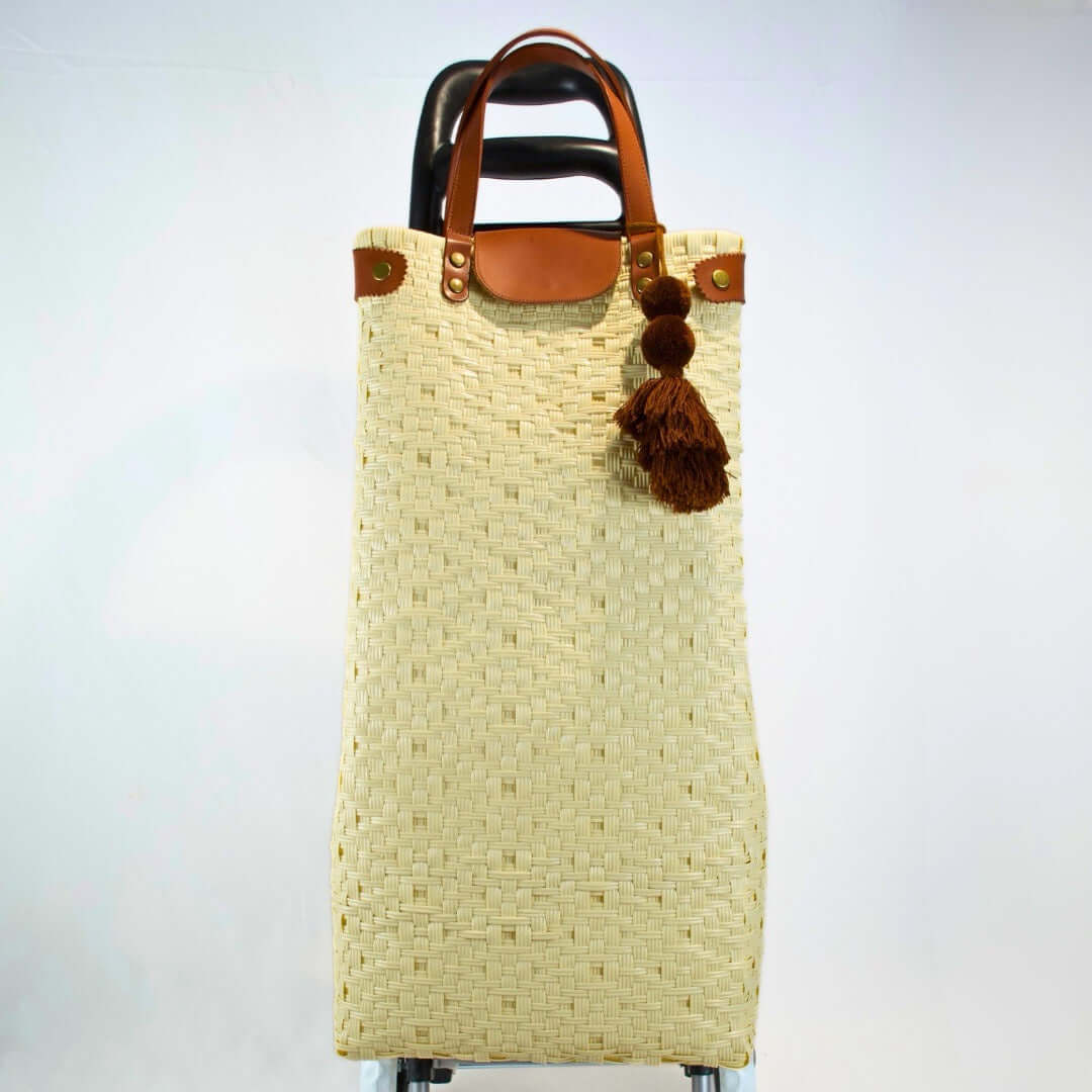 Bolsa artesanal para mandado color natural, tejida a mano con toquilla obtenida del reciclado de plástico. Incluye detalles y asas en piel sintética color café, con accesorios decorativos tejidos. Diseño funcional y elegante para uso diario, hecho en México con material plástico reciclado, toquilla, tejida en penales mexicanos.