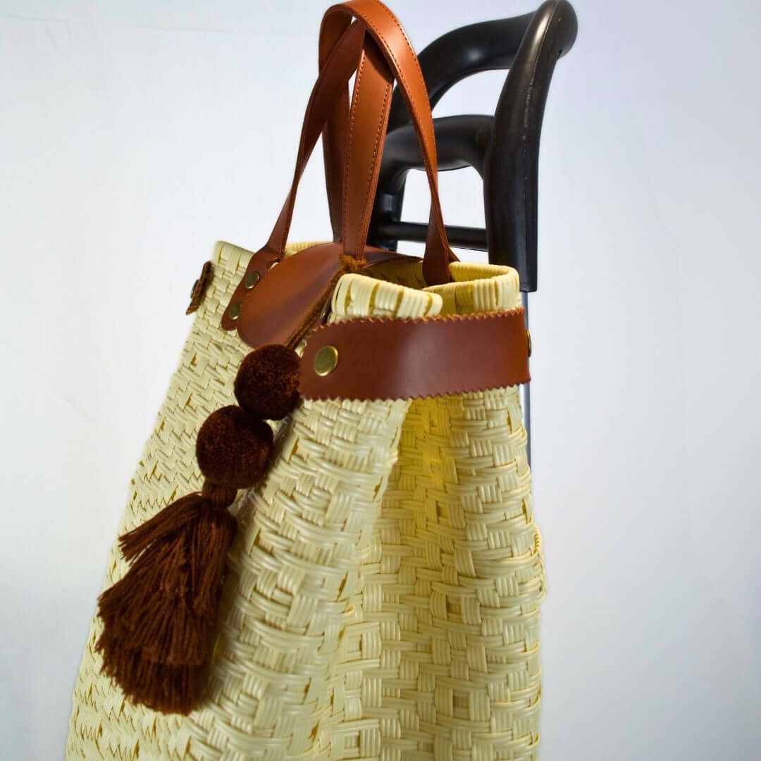 Bolsa artesanal para mandado color natural, tejida a mano con toquilla obtenida del reciclado de plástico. Incluye detalles y asas en piel sintética color café, con accesorios decorativos tejidos. Diseño funcional y elegante para uso diario, hecho en México con material plástico reciclado, toquilla, tejida en penales mexicanos.